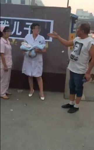 医生抱着幼儿的尸体和护士站在医院大门前