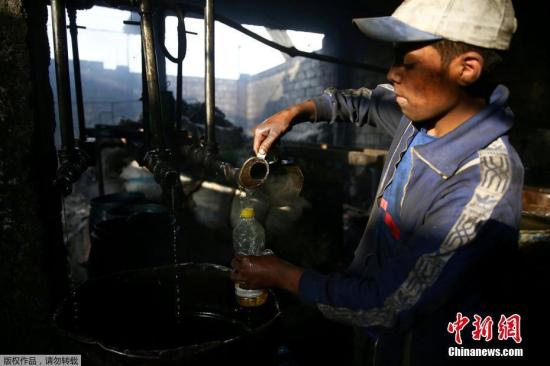 资料图：叙利亚工人自己建设炼油厂，应对燃料短缺。图为一名男子在车间检查燃料。