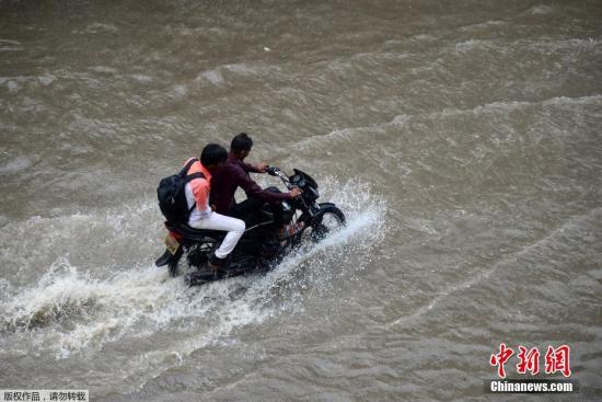 资料图：印度进入雨季，民众骑摩托车经过被大水淹没的街道。