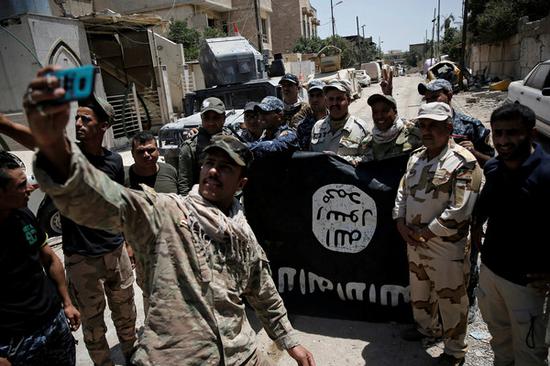 伊拉克收复摩斯尔后，官兵们开心捡起“伊斯兰国”旗帜拍照。（图片来源：路透社）