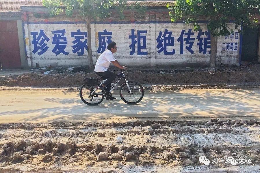  新华区津德公路，一名男子骑着自行车经过一面“拒绝传销”宣传标语墙。