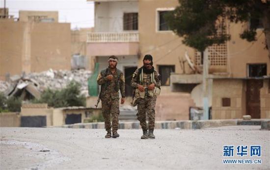 资料图：在叙利亚拉卡附近的塔卜卡镇，两名“叙利亚民主军”士兵走在街道上。