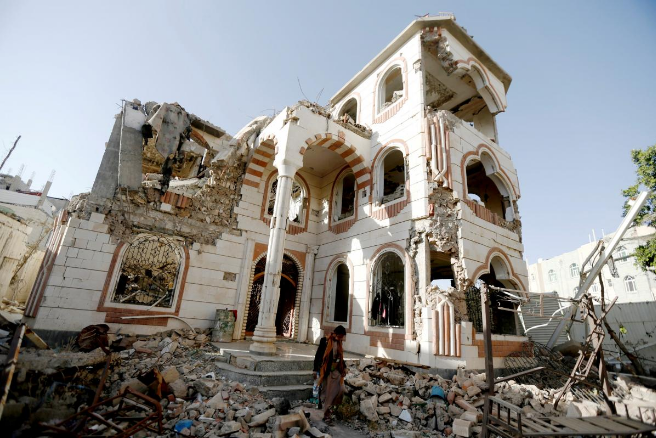 2018年3月21日，也门首都萨那，一名警卫走在被空袭毁坏的房屋的院子里。（图源：路透社）