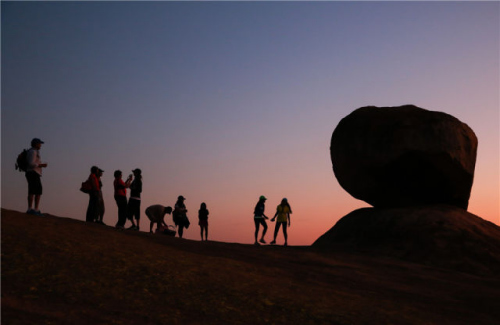 2015年11月9日，在哈拉雷东坡莎瓦山上，几名游客在一处平衡石景点旁边观赏日落。新华社发 王新举摄