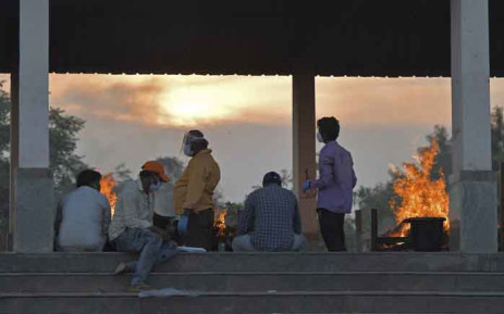 People are seen next to burning pyres of victims who lost their lives due to the COVID-19 coronavirus at an open crematorium in Bangalore, India, on 26 April 2021. Picture: Manjunath Kiran/AFP