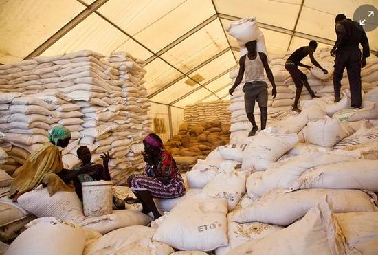 ▲在南苏丹的世界粮食计划署分发点，男人们负责扛食物，女人们等着分发食物。图据路透社